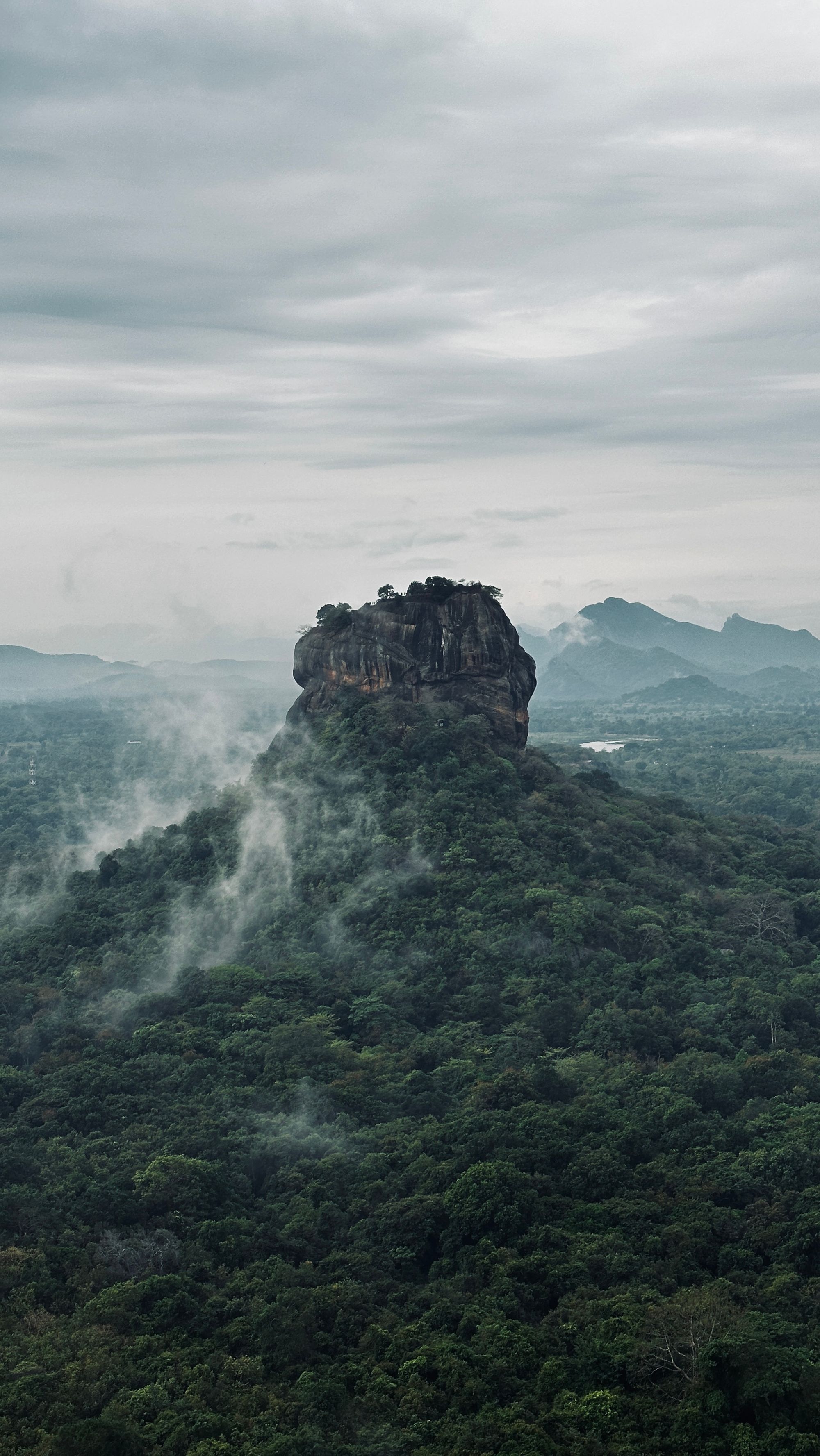 Sigiriya rock rising through mist above the surrounding forest